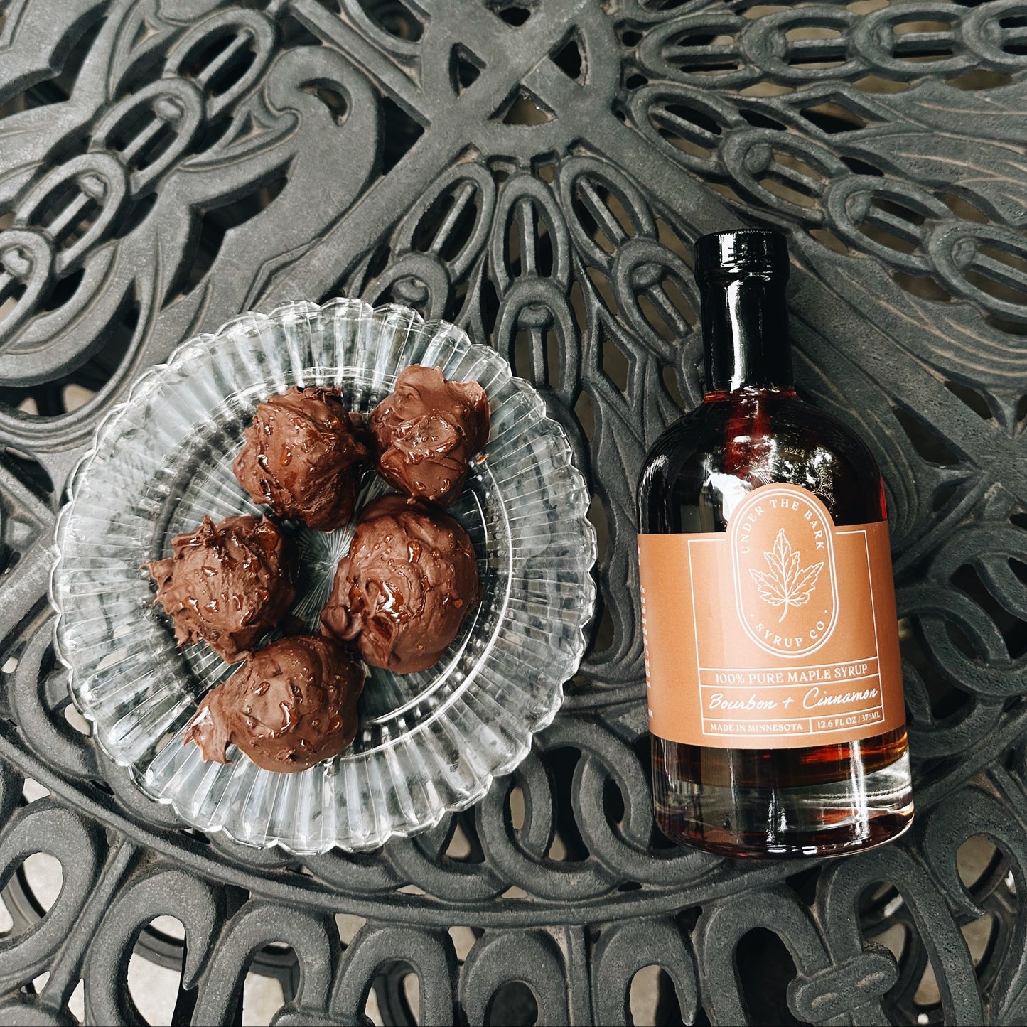 
                  
                    Bottle of bourbon maple syrup with a dessert on a decorative metal surface
                  
                