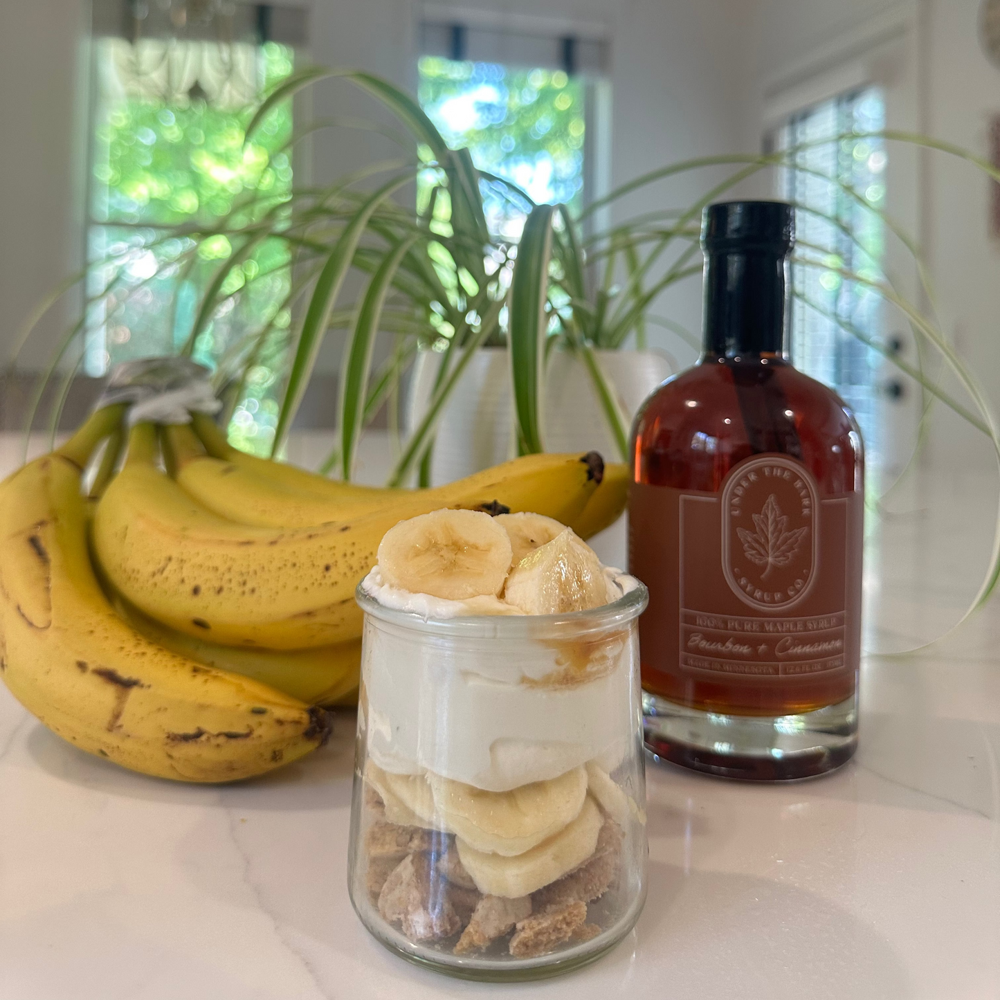 
                  
                    Bananas, a jar of cookies and cream, and a bottle of bourbon cinnamon maple syrup on a kitchen counter.
                  
                