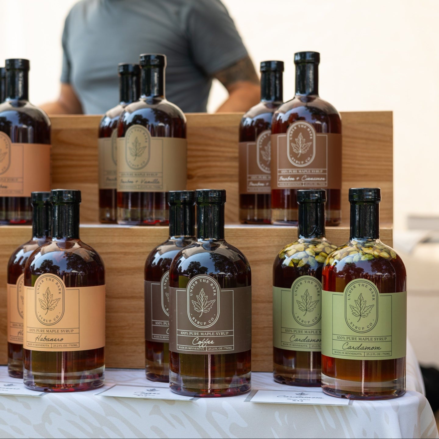 
                  
                    Bottles of maple syrup on a table with a person in the background
                  
                